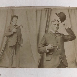 Può includere: Due uomini in abito e cappello, uno con un bastone e l'altro che fa un inchino.