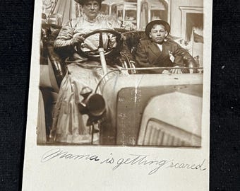 Può includere: Fotografia vintage in bianco e nero di una donna e un ragazzo in un'auto. La donna indossa un grande cappello e tiene il volante. Il ragazzo indossa un cappello e un abito. Il testo "Mama is getting scared" è scritto in basso.