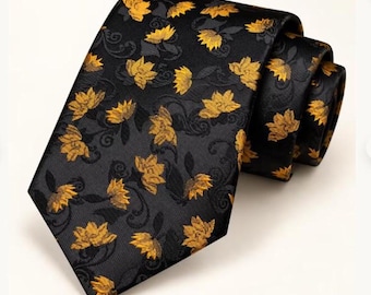 May include: A black necktie featuring a repeating pattern of golden yellow lotus-like flowers and dark gray swirling vine motifs. The fabric has a subtle diagonal weave texture, and the tie is shown partially rolled to display the design.
