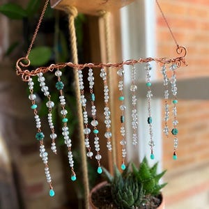 May include: A hanging suncatcher featuring a twisted copper wire frame with ten dangling strands of clear faceted glass beads and small turquoise-colored accents. The strands vary in length and are finished with small turquoise teardrop beads.