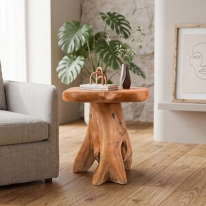 May include: A side table crafted from a single piece of light brown natural wood, featuring a thick, smooth, rounded tabletop supported by a sturdy, organic tree stump base with visible wood grain patterns and natural knots throughout the structure.