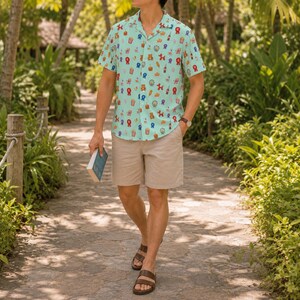 May include: A light blue short-sleeve button-down shirt featuring a repeating pattern of colorful carnival-themed icons including red ribbons, popcorn buckets, and balloon animals, paired with beige shorts and brown leather sandals.