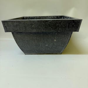 May include: A square-shaped planter with a galvanized metal finish. The container features a wide, flat rim and tapered sides that narrow toward the base. The surface has a mottled, industrial gray texture characteristic of galvanized steel.