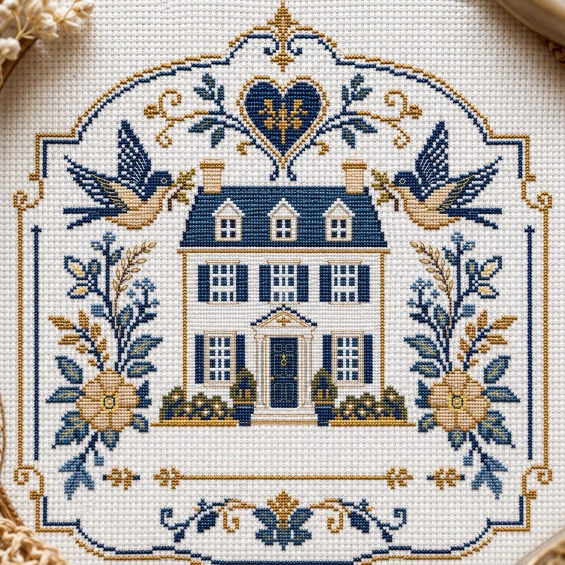Puede incluir: Un patr&oacute;n de punto de cruz sobre tela blanca que presenta una casa central de dos pisos con contraventanas azules y una puerta oscura. El dise&ntilde;o est&aacute; enmarcado por dos p&aacute;jaros, arreglos florales y un motivo de coraz&oacute;n en tonos azul y oro.