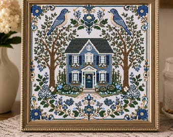 Puede incluir: Un bordado en punto de cruz enmarcado que presenta una casa azul centrada entre dos árboles con pájaros azules posados en las ramas. El diseño incluye motivos florales, follaje verde y bordes decorativos en tonos azules, marrones y verdes sobre un fondo de tela blanca.