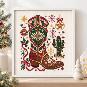 May include: A framed cross-stitch embroidery featuring a central cowboy boot decorated with green, red, and brown patterns, surrounded by holiday motifs including snowflakes, a decorated cactus, a star ornament, and holly sprigs.