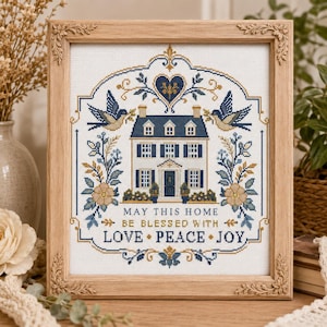Puede incluir: Un bordado en punto de cruz enmarcado que presenta una casa central con contraventanas azules, flanqueada por p&aacute;jaros y motivos florales. El texto dice: MAY THIS HOME BE BLESSED WITH LOVE PEACE JOY. Dise&ntilde;o con hilos azul, dorado y blanco sobre tela blanca.