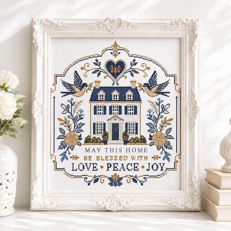 Puede incluir: Un bordado en punto de cruz enmarcado que presenta una ilustraci&oacute;n central de una casa rodeada de p&aacute;jaros, motivos florales y un coraz&oacute;n. El texto dice: MAY THIS HOME BE BLESSED WITH LOVE PEACE JOY. El dise&ntilde;o usa una paleta de azul marino, oro y blanco.