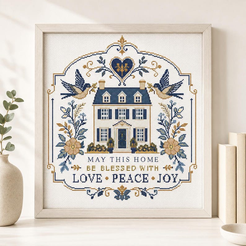 Puede incluir: Un bordado en punto de cruz enmarcado que presenta una ilustraci&oacute;n de una casa, dos p&aacute;jaros, motivos florales y el texto: MAY THIS HOME BE BLESSED WITH LOVE &bull; PEACE &bull; JOY. El dise&ntilde;o utiliza una paleta de azul marino, beige y blanco.