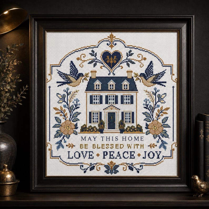 Puede incluir: Un bordado en punto de cruz enmarcado que presenta una ilustraci&oacute;n central de una casa flanqueada por dos p&aacute;jaros, motivos florales y un coraz&oacute;n en la parte superior. El texto dice: MAY THIS HOME BE BLESSED WITH LOVE PEACE JOY. Hilo azul marino, dorado y blanco.