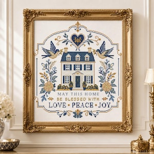 Puede incluir: Un bordado de punto de cruz en un marco dorado ornamentado que presenta una casa, p&aacute;jaros y motivos florales en azul y oro. El texto dice: MAY THIS HOME BE BLESSED WITH LOVE PEACE JOY. El dise&ntilde;o est&aacute; centrado sobre un fondo de tela blanca.