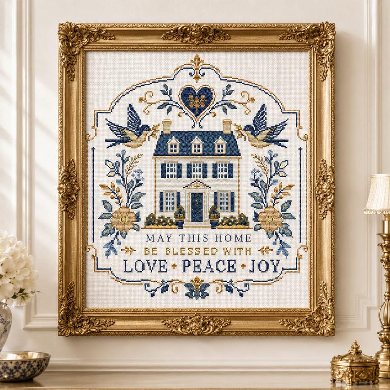 Puede incluir: Un bordado de punto de cruz en un marco dorado ornamentado que presenta una casa, p&aacute;jaros y motivos florales en azul y oro. El texto dice: MAY THIS HOME BE BLESSED WITH LOVE PEACE JOY. El dise&ntilde;o est&aacute; centrado sobre un fondo de tela blanca.