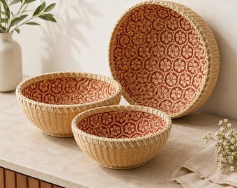 May include: Three round woven baskets of varying sizes, each featuring a light tan exterior and a deep red interior lining decorated with a repeating white floral pattern. The baskets are arranged in a cluster, showcasing their circular shape.