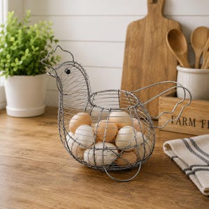 May include: A chicken-shaped wire basket made of thin silver-toned metal, featuring a detailed head and tail design. The basket is filled with a collection of whole brown and white eggs, showcasing a structured grid pattern throughout the frame.