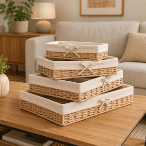 May include: A set of four rectangular woven wicker storage baskets stacked in descending order of size. Each basket features a light beige fabric liner that folds over the top edge and is decorated with a small, tied fabric bow at the center.