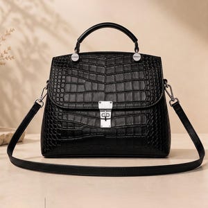 Könnte beinhalten: Eine schwarze Handtasche mit Krokodilleder-Textur, ausgestattet mit einem Tragegriff, einem abnehmbaren Schulterriemen und einem silberfarbenen Drehverschluss an der Frontklappe. Die Tasche hat eine strukturierte Form mit silbernen Beschlägen.
