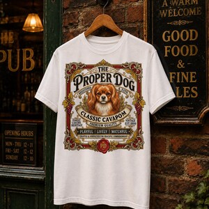 Puede incluir: Una camiseta blanca con un estampado gráfico de un perro marrón y blanco centrado dentro de una etiqueta ornamentada de estilo vintage. El texto dice The Proper Dog, Classic Cavapom, Premium Quality, Playful, Lively, Watchful y Est. 1899.