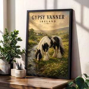 Può includere: Una stampa artistica incorniciata raffigurante un cavallo Gypsy Vanner bianco e nero che pascola vicino a un ruscello in un paesaggio irlandese verdeggiante. Il testo GYPSY VANNER IRELAND è stampato in nero in alto. Include colline e un cottage.