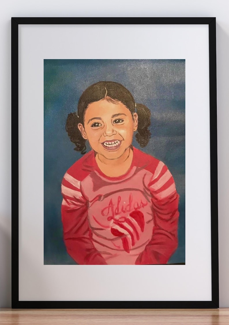 May include: A framed painting of a smiling child with dark hair in pigtails, wearing a long-sleeved pink and red shirt with the word Adidas and a red graphic logo printed on the front, set against a solid dark blue background.