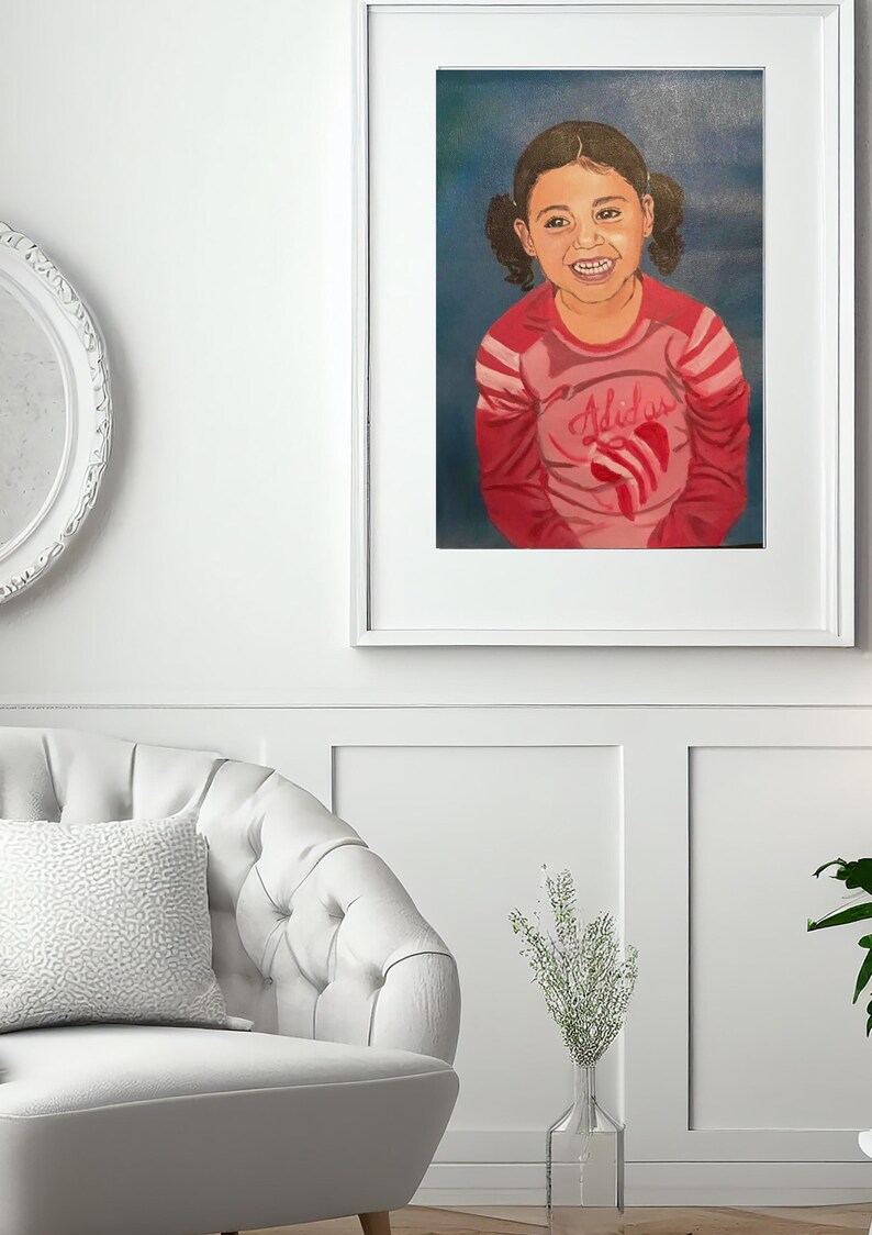 May include: A framed portrait painting of a smiling child with dark hair in pigtails. The child wears a long-sleeved pink shirt with red stripes on the sleeves and a red heart graphic on the chest. The background is a solid dark blue color.