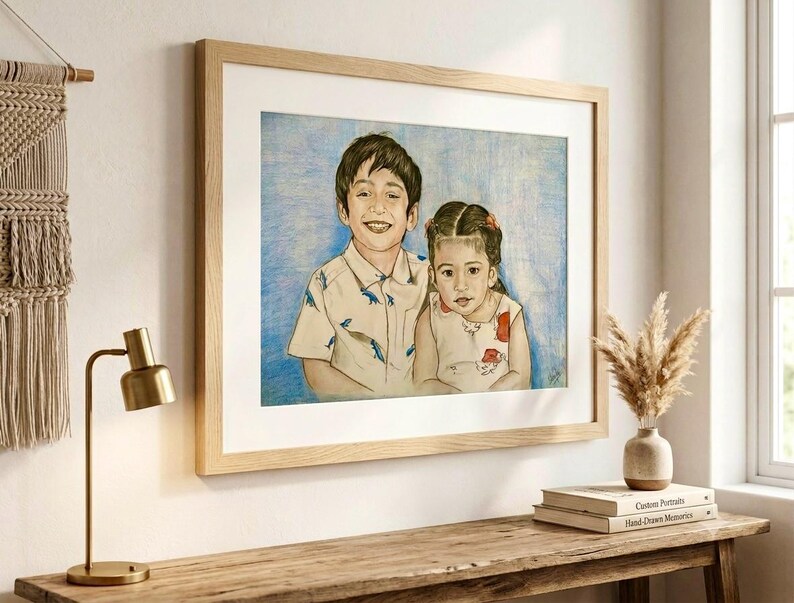 May include: A framed colored pencil portrait of a young boy and a young girl. The boy wears a light-colored short-sleeved shirt with a blue dinosaur pattern. The girl wears a light-colored sleeveless top with a red floral pattern. The background is blue.