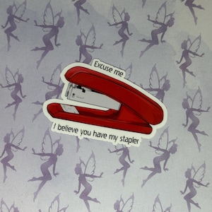 May include: A red stapler sticker with the text "Excuse me, I believe you have my stapler." The sticker is on a background with purple fairy silhouettes. Office supplies.