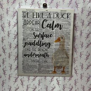 May include: A white duck with a yellow beak is superimposed on a vintage dictionary page. The text on the page reads "Be like a duck, appear calm on the surface but paddling like the dickens underneath." The quote is attributed to Michael Caine.