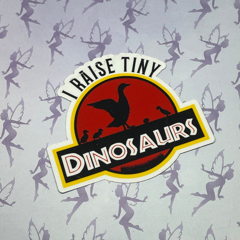 May include: A yellow and red sticker with the text "I raise tiny dinosaurs" and a cartoon image of a duck and ducklings. The sticker is on a purple background with a pattern of fairies.