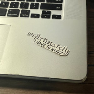 Pu&ograve; includere: Un adesivo bianco e nero con il testo "purtroppo devo preoccuparmi" su un laptop argentato.