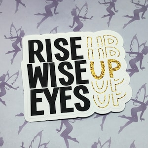 May include: White sticker with black text that reads "Rise Wise Up Eyes" and gold glitter text that reads "Up" multiple times.
