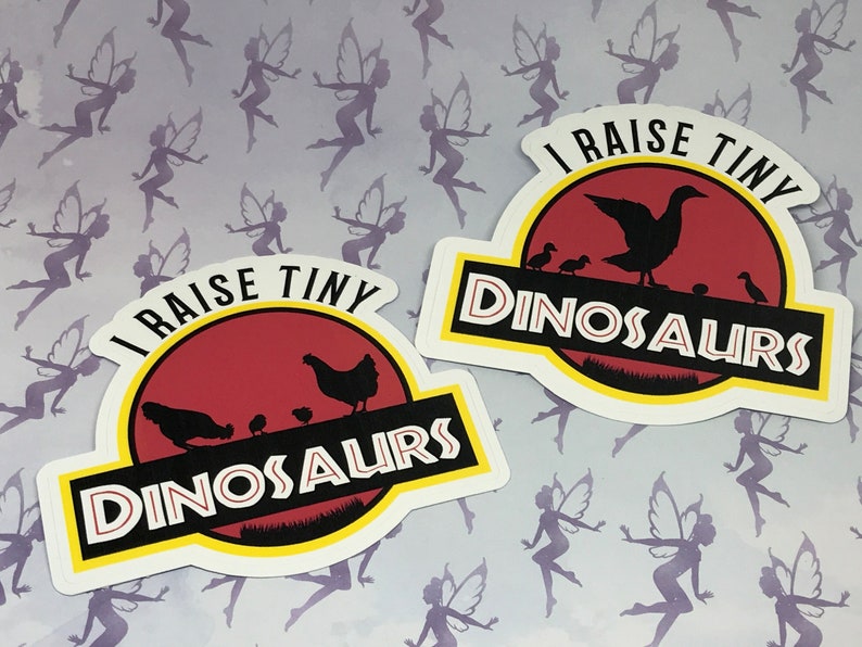 May include: Two stickers with a red, yellow, and black dinosaur silhouette design. The text on the stickers reads "I raise tiny dinosaurs".