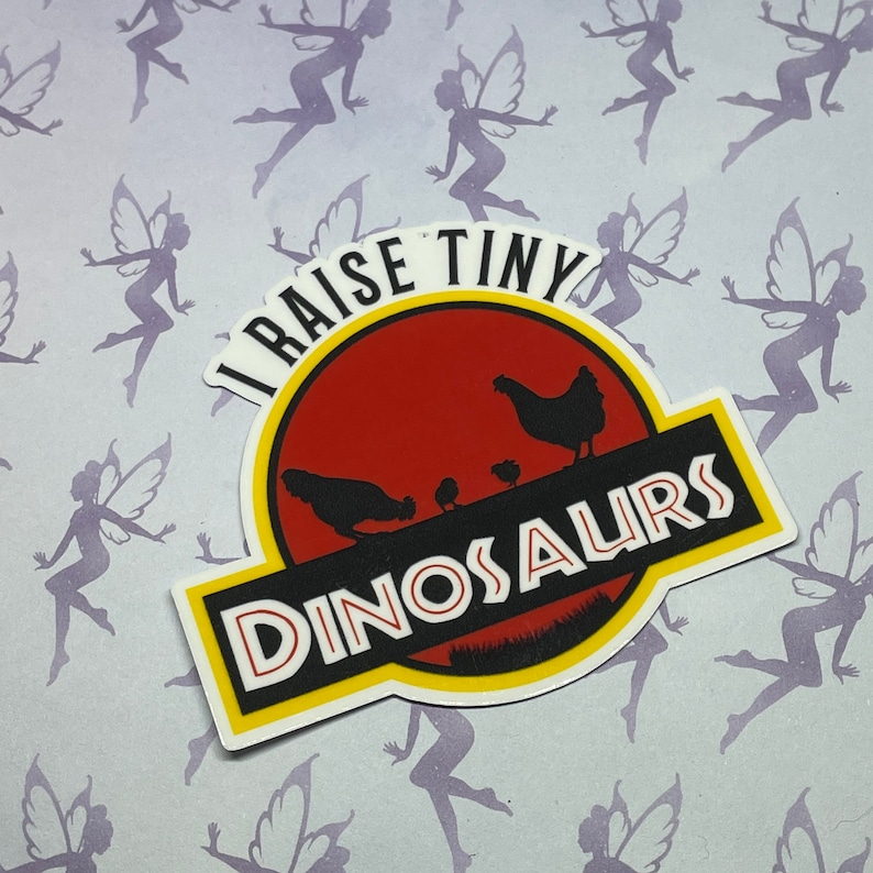 May include: A white sticker with a red, yellow, and green Jurassic Park-style logo. The logo says "I raise tiny dinosaurs" with a silhouette of a mother chicken and chicks inside.