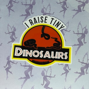 May include: A yellow, red, and black sticker with the text "I raise tiny dinosaurs" and a silhouette of two snakes.