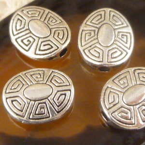 May include: Four silver oval-shaped beads with a decorative geometric pattern. The beads have a hole in the center for stringing.