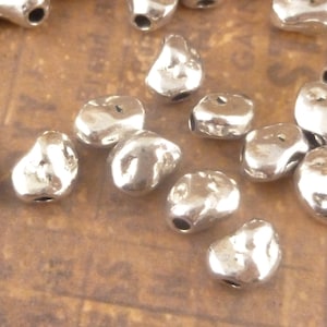 May include: A collection of silver-toned metal beads with a rough, irregular texture. The beads are small and have a hole in the center for stringing.