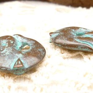 May include: Two copper-coloured buttons with a turquoise patina. The buttons are shaped like a fish with a hole in the middle.