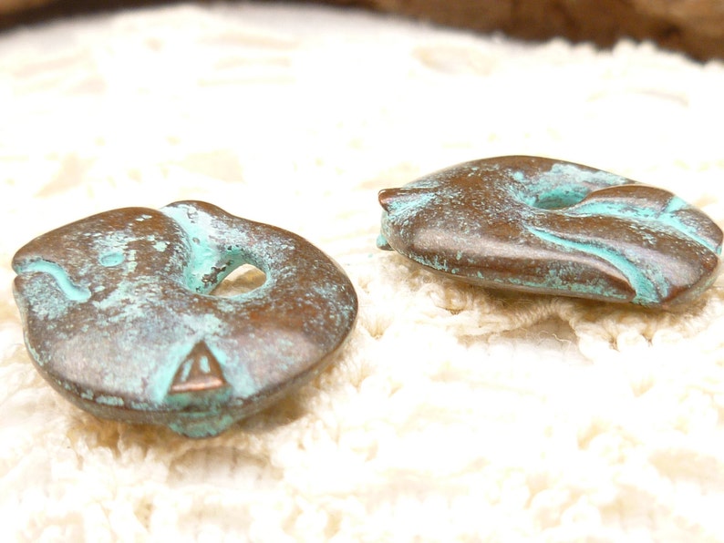 May include: Two copper-coloured buttons with a turquoise patina. The buttons are shaped like a fish with a hole in the middle.