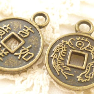 May include: Two antique bronze-colored coin pendants. One coin features Chinese characters around a square center hole. The other coin has a dragon design around a square center hole. Both pendants have a small loop at the top.