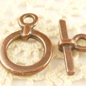 Può includere: Un paio di chiusure in metallo color rame antico per la creazione di gioielli. La chiusura a sinistra ha un anello rotondo e una barra decorativa. La chiusura a destra ha una barra dritta e un piccolo anello.