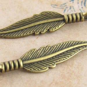 May include: Two antique gold-toned metal feather charms with a detailed etched design. Each charm has a loop at the top for attaching to jewelry or other crafts.