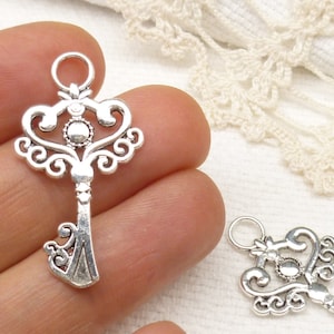 May include: Two silver ornate key charms with a decorative swirl design. The keys have a loop at the top for attaching to a necklace or bracelet.