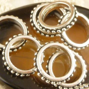 May include: A set of silver jump rings with a beaded edge. The rings are stacked and overlapping, creating a decorative and intricate design.