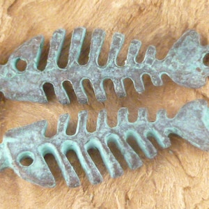 May include: Two turquoise blue metal fish bone charms. The charms are detailed with a textured finish and have a hole at the top for attaching to jewelry.