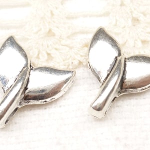 May include: Two silver-toned metal charms shaped like a fish tail. The charms are detailed with a curved line down the center and have a smooth, shiny finish.