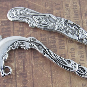May include: Two silver bookmark pendants with detailed designs. One features a dolphin jumping out of the water, the other has a stylized fish design.