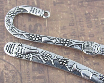 May include: Two silver metal bookmarks with a wine bottle and grapes design. The bookmarks are shaped like a hook and have a detailed design.