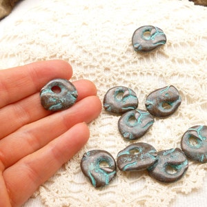 May include: A collection of ten turquoise and brown metal beads with a hole in the centre. The beads are irregularly shaped and have a rustic, aged look.