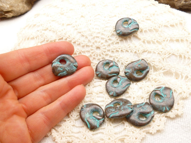 May include: A collection of ten turquoise and brown metal beads with a hole in the centre. The beads are irregularly shaped and have a rustic, aged look.