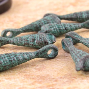 May include: Close-up of several small, antique-style metal charms. Each charm is a teardrop shape with a loop at one end and a textured surface, finished in shades of green and brown. These charms are ideal for jewelry making.