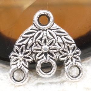 May include: Silver-toned metal charm with three loops and a floral design. The charm features three stylized flowers with leaves.